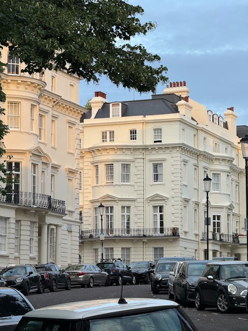 A wide view of a multi-storey, white terraced building with ornate architectural details, including decorative window frames, small balconies, and columns at the entrance, situated along a city street