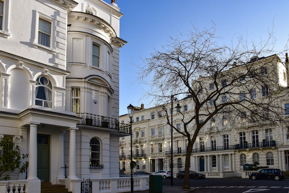 Newly built white Victorian-style terraced houses with ornate black iron railings and small balconies, situated along a tree-lined street in Belgravia, London. Several cars, including a silver estate